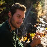 Adrian Hallberg, founder of Kindred Content, outdoors in autumn light beside a film camera on a small tripod