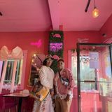 Arlesia and Letecia Whitaker, co-founders of TBOM Apparel, together inside a pink cafe beneath a neon Welcome to Our Happy Place sign