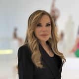 Carole Feuerman, American superrealist sculptor, in a black jacket in a gallery with her swimmer sculptures behind her