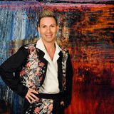 Corey Locke, founder of Aristotle Cosmetics, in a white shirt and floral-embroidered black jacket in front of a painted backdrop