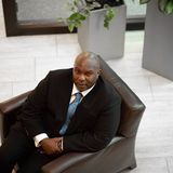 Devord J. Allen, founder of Breaking Barriers Inc., seated in a leather armchair in a suit and blue tie