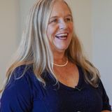 Dianne Allen, founder of Visions Applied, laughing in a navy top and pearl necklace