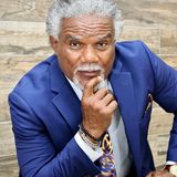 Donald L. Dowridge, Jr., founder of DLD Enterprises, in a royal blue suit and paisley tie, resting his chin on his hand