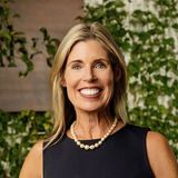 Emily Fournier, founder of Emily’s Table, smiling in a navy dress and pearl necklace in front of a green ivy wall