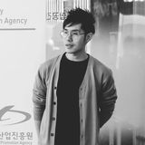 Gregory Tan, composer and founder of Soul Forest Music, in glasses and a grey cardigan at the Busan sync music conference, black and white