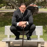 Jacob Sneed, founder of Incendiary Concepts, seated on a stone bench in a dark suit with a walking cane