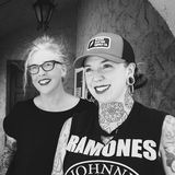 Heather Reynolds and Kate Grinstead, co-founders of Zeitgeist Tattoo, smiling side by side under a stucco archway in black and white