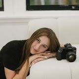Kate Thayer, founder of Captured by Kaitlyn, resting her head on her arms on a white sofa beside her Canon film camera