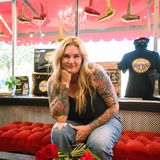 Machele Alessandrine, owner of Lux and Roses, sitting in her salon window with a bouquet of red roses, hair dryers hanging overhead