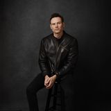 Michael Cecchinelli, founder of Solveig Pictures, seated on a stool in a black leather jacket against a dark studio backdrop