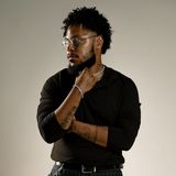 Remy Janvier, founder of JanviFX Studios, in a black long-sleeve top and wire-rimmed glasses, looking to the side with a hand at his collar