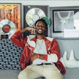 Sean "Kid Flvsh" Williams, founder of Flash FWD Productions, smiling on a sofa in a red and white jacket in front of framed platinum records