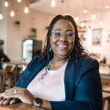 Dr. Sharon M. Jones, founder of My 3 Tiers Emotional Clarity, smiling in glasses and a navy blazer at a wooden table in a cafe