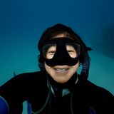 Shera Mercer, founder of ʻAlohi Kai, smiling underwater in a dive mask and wetsuit