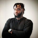 Simpa Samson, documentary filmmaker and founder of VisualFarm Production, arms crossed in a black shirt against a pale wall