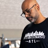 Sri Gadde, founder of CarDoctorATL, in glasses and a Car Doctor ATL t-shirt working on a part in gloves