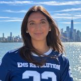 Sydney Kessler, founder of EMS Revolution, in a navy EMS Revolution jersey on the Hudson waterfront with the Manhattan skyline behind her