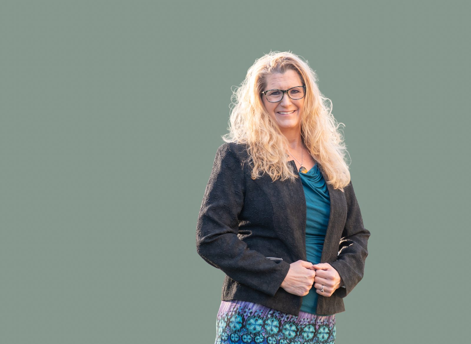 Dr. Tobi Jeurink, founder of Root Function Health, smiling in a black jacket and teal top against a sage green backdrop