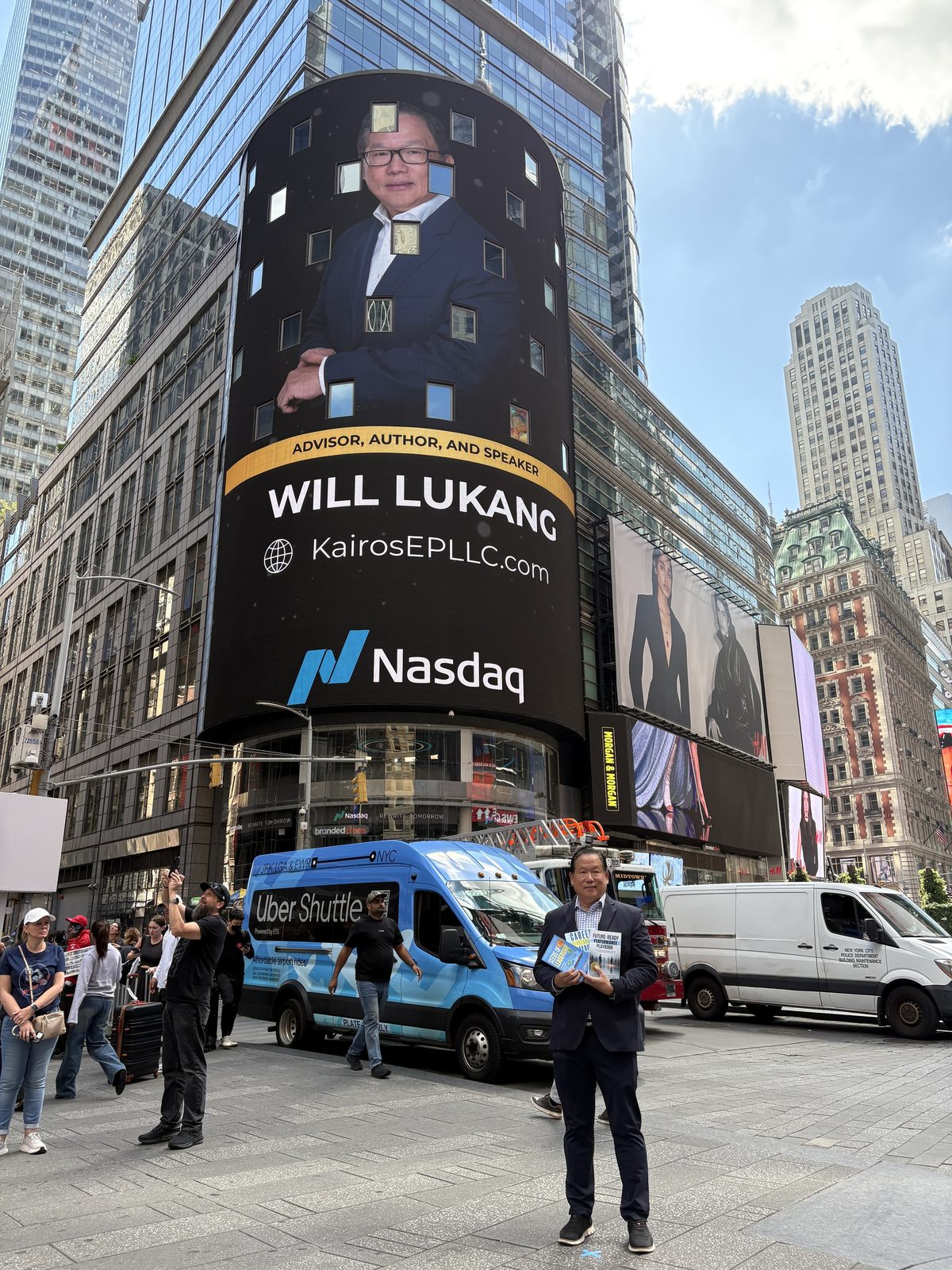 Will Lukang standing in Times Square in front of the Nasdaq tower, which is displaying his name and the Kairos Elite Partnership website